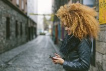 Donna sorridente con i capelli afro guardando il suo smartphone — Foto stock