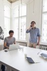Dos empresarios creativos con portátil y teléfono celular en una oficina moderna - foto de stock