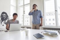 Dos empresarios creativos con portátil y teléfono celular en una oficina moderna - foto de stock