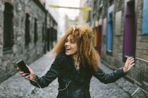 Happy woman with afro hair hearing music with smartphone and earbuds — Stock Photo