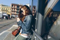 Donna alla fermata dell'autobus con un cellulare in mano — Foto stock