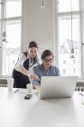 Два креативных профессионала, работающих на ноутбуке в современном офисе — стоковое фото