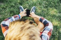 Мальчик-подросток сидит на лугу со смартфоном — стоковое фото