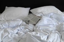 Rumpled white bed with glasses and newspaper — Stock Photo