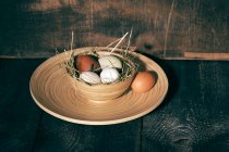 Nido de Pascua con huevos de colores en un tazón de madera oscura - foto de stock