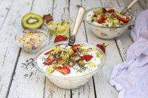 Strawberry kiwi yogurt with cereals, chia seeds, agave syrup in glass bowl on wood — Stock Photo