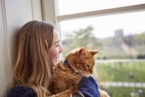 Teenager mit Katze schaut durch Fenster — Stockfoto