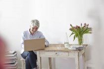 Mujer madura sentada en la mesa usando el portátil - foto de stock