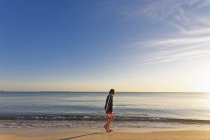 Giovane ragazzo in piedi sulla spiaggia di sabbia con cielo limpido sullo sfondo — Foto stock