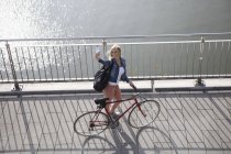 Blond woman with bicycle standing in front of Rhine River taking a selfie with smartphone — Stock Photo
