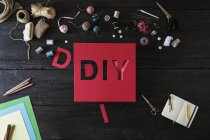 Craft materials and red cardboard with the word DIY on black wood — Stock Photo