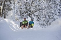 Pareja divirtiéndose en trineos en paisaje cubierto de nieve - foto de stock
