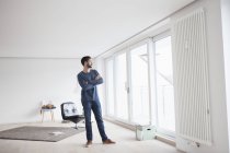 Jeune homme debout dans son salon regardant par la fenêtre — Photo de stock