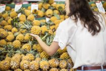 Женщина проверяет ананасы в фруктовом киоске — стоковое фото