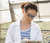 Giovane giardiniere donna che esamina le piante in vivaio — Foto stock