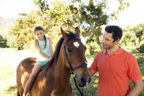 Отец с дочерью сидят на лошади в парке — стоковое фото