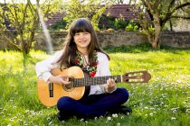 Портрет улыбающейся девушки на лугу, играющей на гитаре — стоковое фото