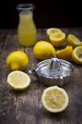 Presse-citron et citrons frais avec cruche de jus sur bois foncé — Photo de stock
