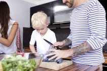 Hombre cortando repollo rojo en la cocina mientras su hijo mira - foto de stock