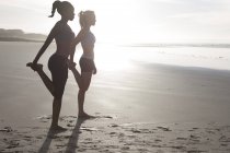 Deux femmes faisant des exercices d'étirement sur la plage au contre-jour — Photo de stock