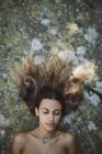 Portrait d'une femme aux yeux fermés couchée sur un rocher aux cheveux touffus — Photo de stock