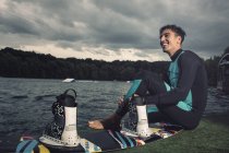 Rilassato giovane wakeboarder seduto sulla riva del lago — Foto stock