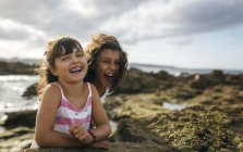 Spain, Gijon, portrait of two laughing little girls at rocky coast — Stock Photo