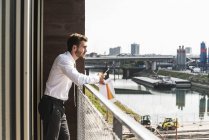 Молодой бизнесмен стоит на балконе и смотрит на вид — стоковое фото