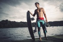 Young wakeboarder standing with his equipment at lakeshore — Stock Photo