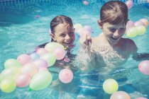 Счастливые мальчик и девочка в бассейне в окружении воздушных шаров — стоковое фото