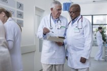 Dos doctores en el pasillo del hospital discutiendo el expediente del paciente - foto de stock