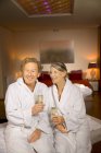 Couple aîné souriant en peignoirs tenant des verres de champagne — Photo de stock