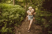 Ragazza che trasporta il bambino a cavalluccio attraverso una foresta — Foto stock