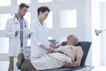 Uomo anziano che fa il check-up in ospedale, infermiera che lo calma — Foto stock