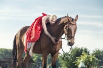 Ritratto di giovane donna vestita con abito da sera rosso seduta a cavallo a forma di cuore con le mani — Foto stock