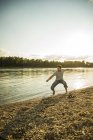 Homme debout au bord de la rivière jetant des cailloux dans l'eau — Photo de stock