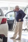 Senior man looking at a new car in showroom — Stock Photo