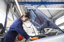 Young woman working in repair garage, checking engine — Stock Photo