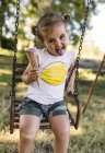 Portrait of little girl with outstretched tongue sitting on a swing eating ice cream — Stock Photo