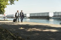 Two young businessmen on a business trip, walking by river — Stock Photo