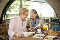 Smiling senior couple reading book and having breakfast in a cafe — Stock Photo