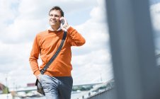 Businessman with shoulder bag walking while talking on the phone — Stock Photo