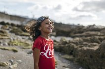 Portrait of smiling little girl on rocky beach looking up — Stock Photo