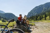 Autriche, Tyrol, Vallée de Tannheim, jeune couple avec VTT et carte assis au ruisseau — Photo de stock