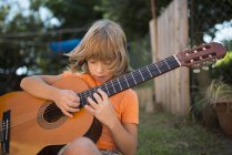 Long-haired blond boy playing spanish guitar outdoors — Stock Photo