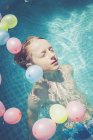 Мальчик в бассейне, окруженный воздушными шарами, плавающими в воде — стоковое фото