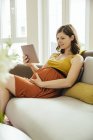 Pregnant woman with digital tablet  relaxing on couch at home — Stock Photo