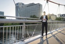 Бизнесмен, стоящая на мосту в сумерках с помощью смартфона — стоковое фото