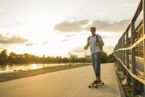Man with coffee to go and smartphone standing on skateboard in the evening twilight — Stock Photo