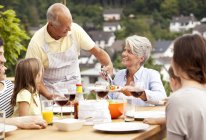 Nonno che serve cibo dal barbecue per la famiglia al tavolo da giardino — Foto stock